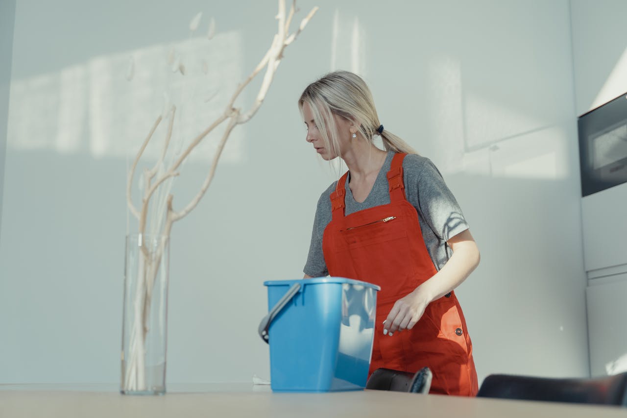 services-03 A woman in a red uniform cleans indoors with a blue bucket, ensuring a spotless environment.