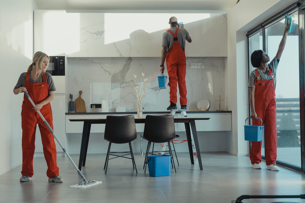 why-choose-us Group of cleaners in red uniforms mopping and wiping glass in a modern dining room.